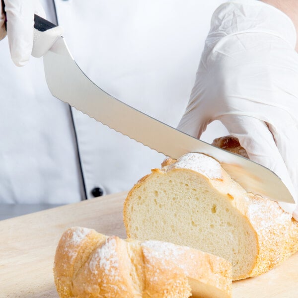 A person wearing white gloves uses a Mercer Culinary Millennia bread knife to cut a loaf of bread.