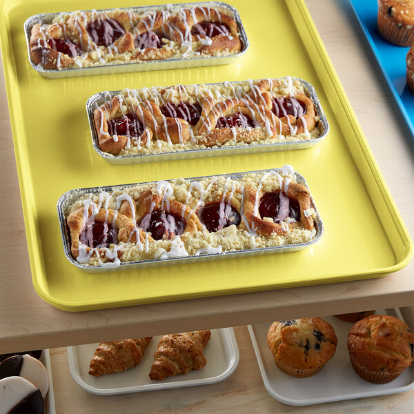 A yellow Cambro market tray on a table with pastries and muffins.