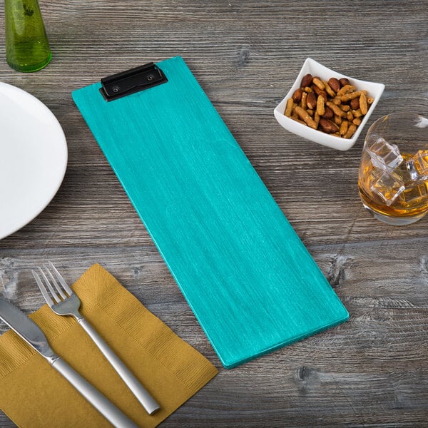 A blue wood clipboard holding a menu next to a plate and a glass of liquid.