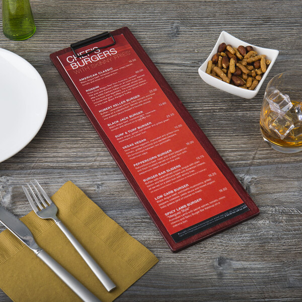 A mahogany wood Menu Solutions clip board on a table with a menu, fork, and knife.