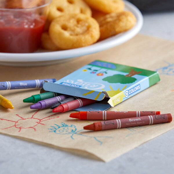 A print box filled with Choice assorted color crayons on a table with a plate of food and crayons.