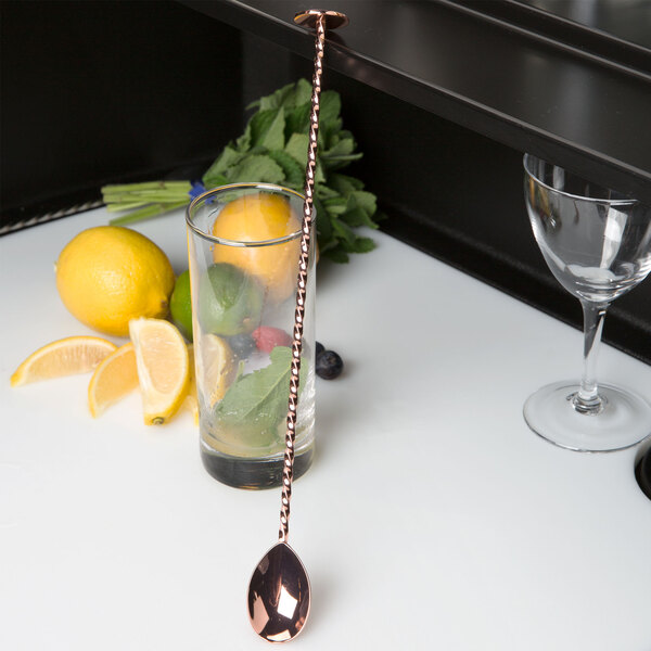 A copper Barfly bar spoon with a muddled lemon in a glass on a counter.