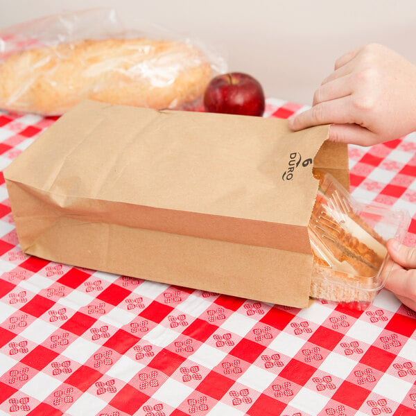 A hand putting a red apple into a Duro brown paper bag.