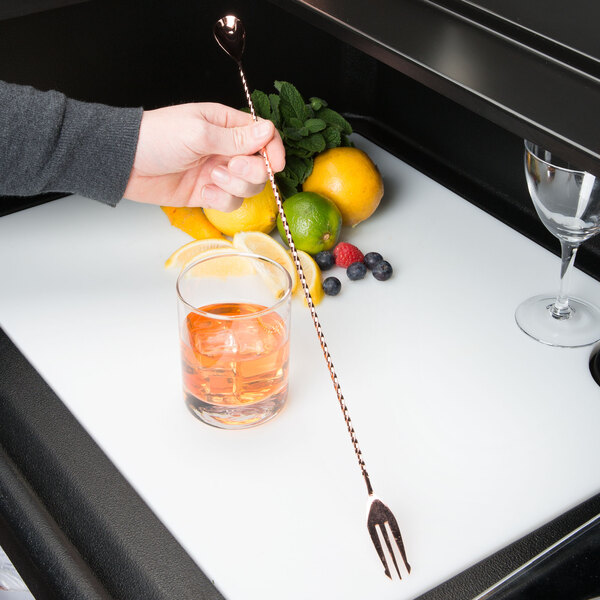 A hand using a Barfly copper plated bar spoon with fork end to garnish a cocktail with a lime.