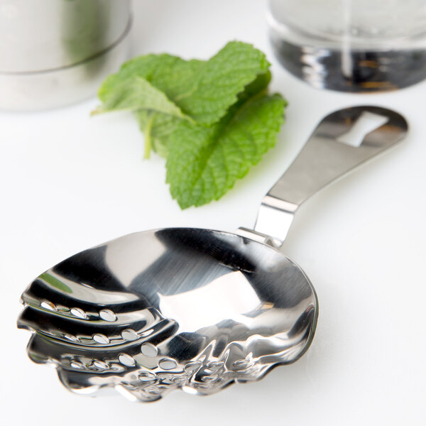 A Barfly stainless steel cocktail strainer with scalloped edges and a mint leaf on it.