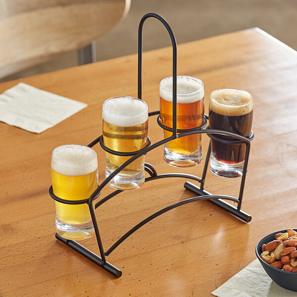 An Acopa metal flight carrier holding four pub tasting glasses of beer on a table in a brewery.