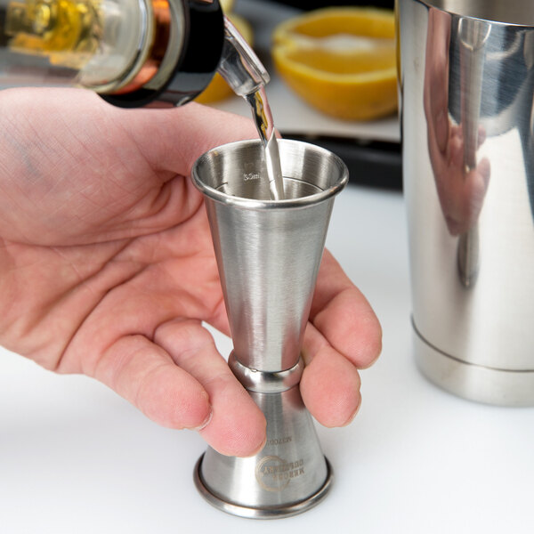 A person using a Barfly stainless steel Japanese style jigger to pour liquid into a metal cup.