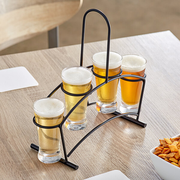 An Acopa metal flight carrier with four flared pilsner glasses of beer on a table.