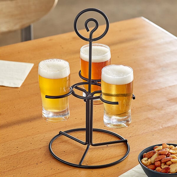 An Acopa metal stand with three pub tasting glasses filled with beer on a table in a brewery.