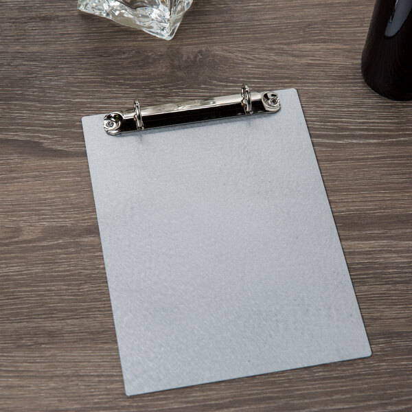 A Menu Solutions aluminum clipboard with two rings on a table.