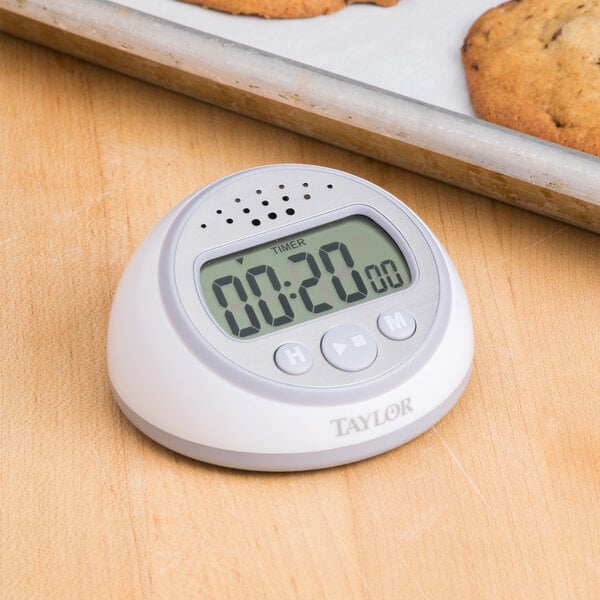 A Taylor digital kitchen timer with clock on a table with cookies.