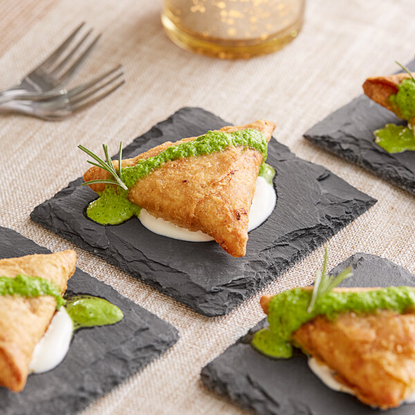 A fried pastry with green sauce on an Acopa black slate plate.