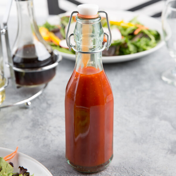 An Arcoroc tinted green glass swing top bottle of liquid on a table in front of a plate of salad.