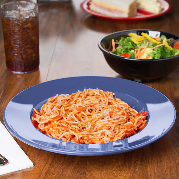 A bowl of spaghetti and salad in a peacock blue melamine bowl on a table.