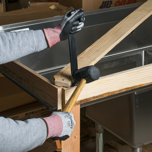 A person wearing Cordova machinist gloves holding a hammer and nailing a piece of wood.