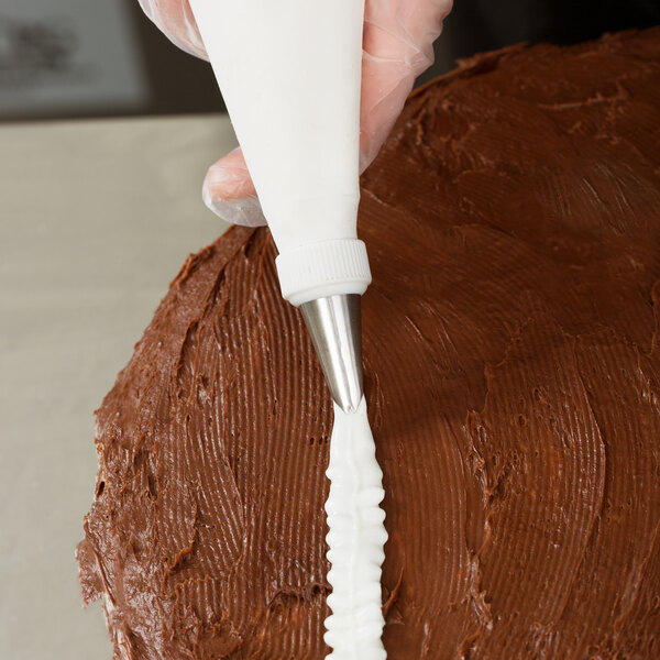 A person using an Ateco leaf piping tip to frost a chocolate cake.