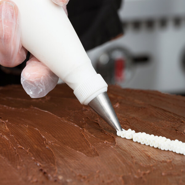 A person's hand uses an Ateco leaf piping tip in a pastry bag to decorate a chocolate cake.