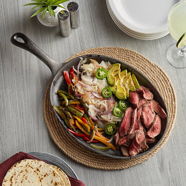 A Valor pre-seasoned cast iron fajita skillet with steak, vegetables and tortillas on a table.