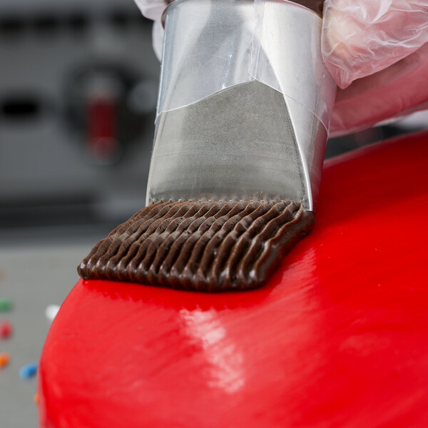 A person using an Ateco 789 metal piping tip to spread chocolate on a cake.