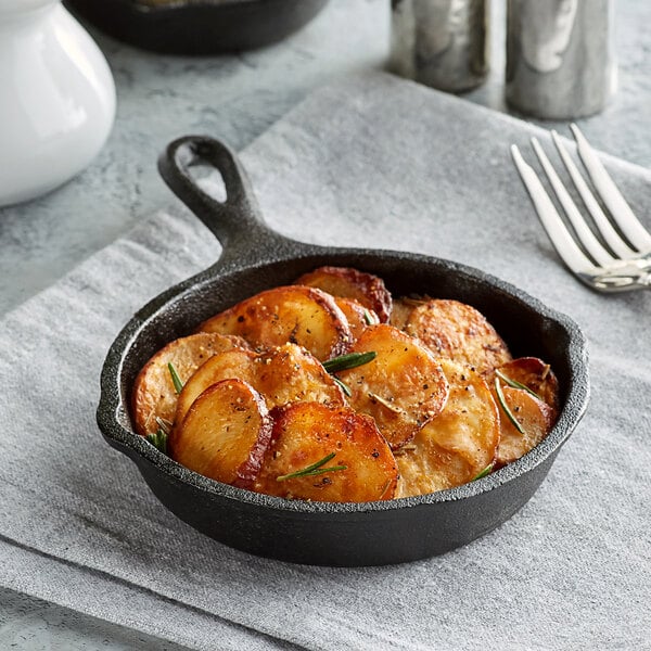 A Valor pre-seasoned mini cast iron skillet filled with potatoes, rosemary, and spices on a table.