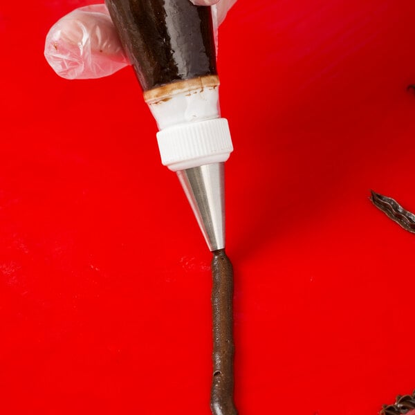A hand using an Ateco plain piping tip to inject brown liquid into a piece of chocolate.