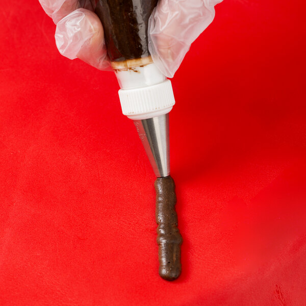 A person holding an Ateco plain piping tip over a pastry bag filled with brown liquid.