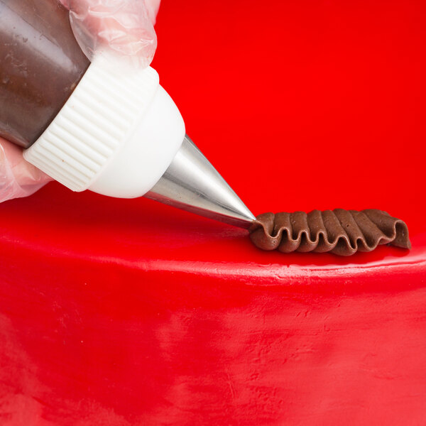 A hand uses an Ateco Rose Leaf piping tip on a pastry bag to pipe frosting on a red cake.
