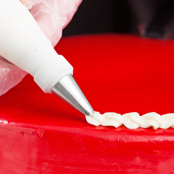 A person using an Ateco leaf piping tip on a pastry bag to decorate a cake.
