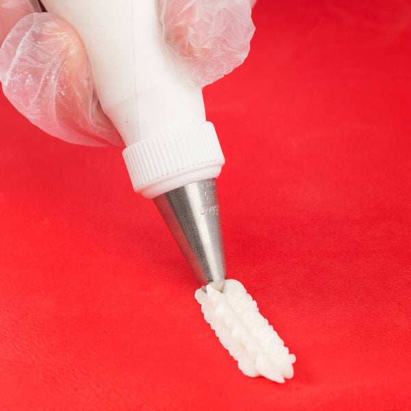 A hand using an Ateco closed star piping tip to pipe frosting onto a tooth.