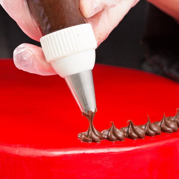 A hand using an Ateco drop flower piping tip to decorate a red cake.
