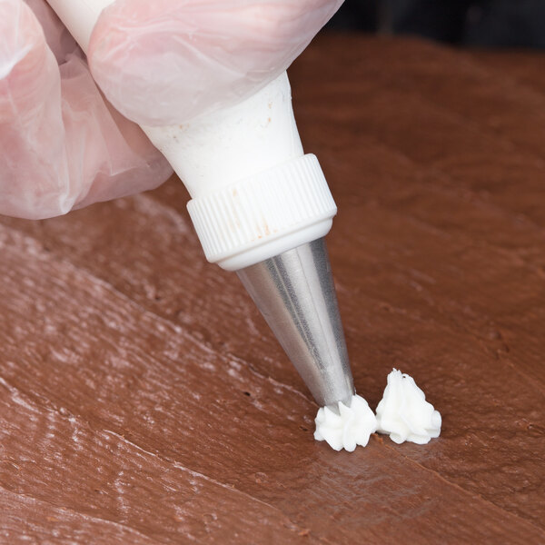 A hand using an Ateco closed star piping tip to frost a cake with a pastry bag.