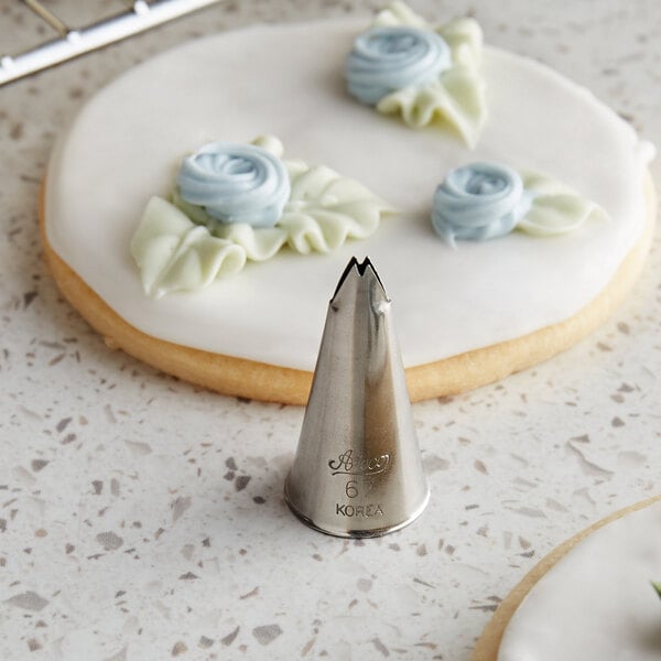 A close up of a metal Ateco leaf piping tip next to a cookie with white icing.