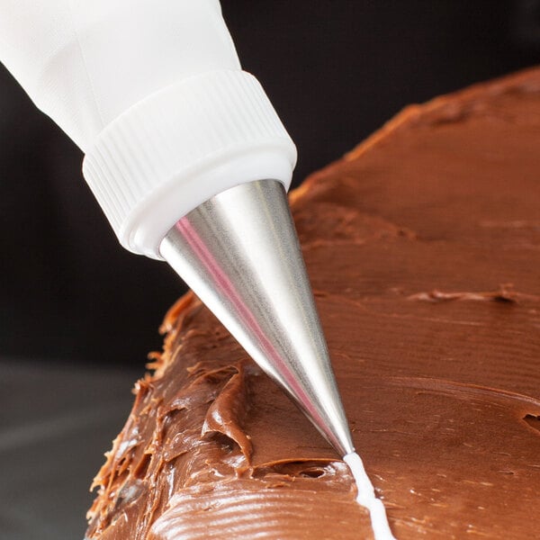 A pastry bag with an Ateco plain piping tip frosting a chocolate cake.