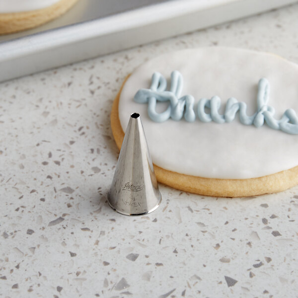 A cookie with "Thank You" written in frosting next to an Ateco plain piping tip.