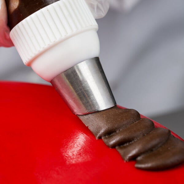 A person using an Ateco U-shape ruffle piping tip to decorate a brown pastry.