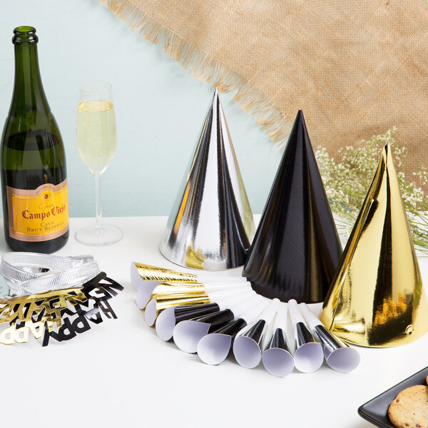 A table with black, silver, and gold New Year's party supplies including party hats and a bottle of champagne.