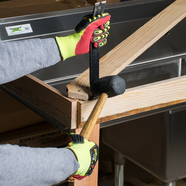 A person wearing Cordova yellow and red heavy duty work gloves holding a hammer and mallet.