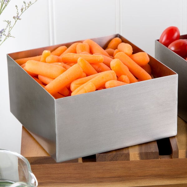 A Tablecraft stainless steel square bowl filled with baby carrots on a counter.