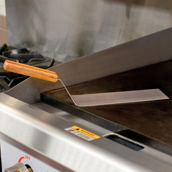 An American Metalcraft solid metal turner with a wooden handle being used on a grill.