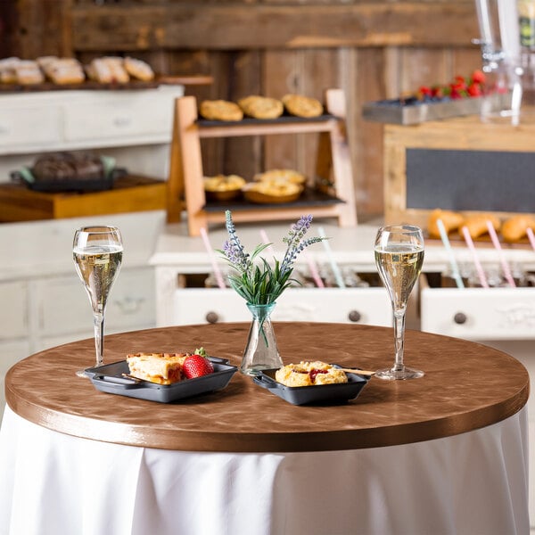 A Tablecraft round translucent copper aluminum table cover on a table with food and drinks.