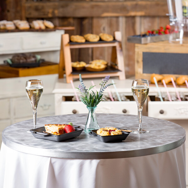 A Tablecraft translucent clear aluminum table cover with food and wine on a round table.