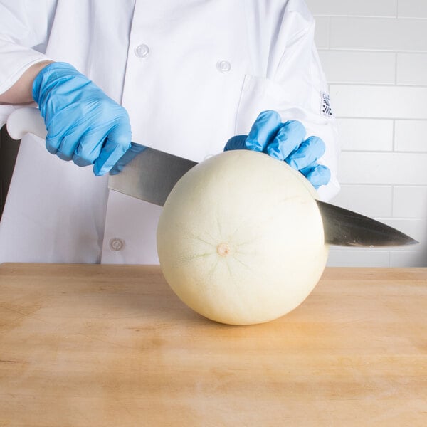 A person in blue gloves using a Choice chef knife to cut a melon.