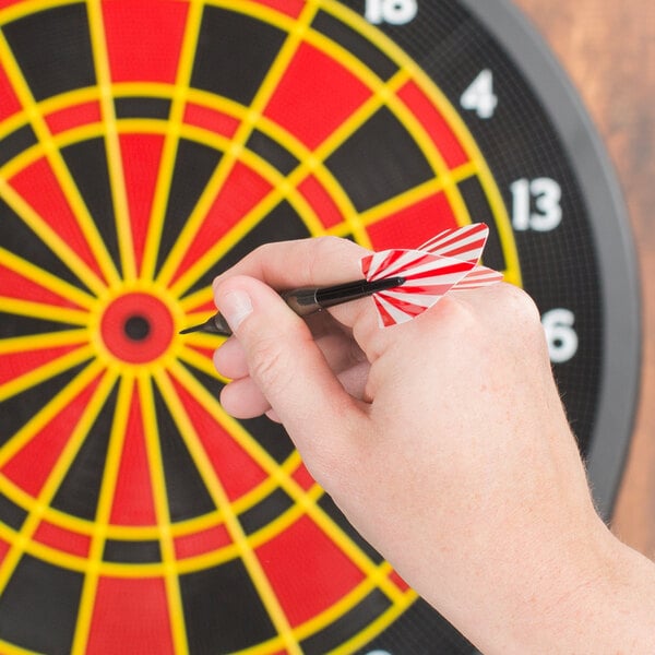 A hand holding an Arachnid red and white soft tip dart in front of a dart board.