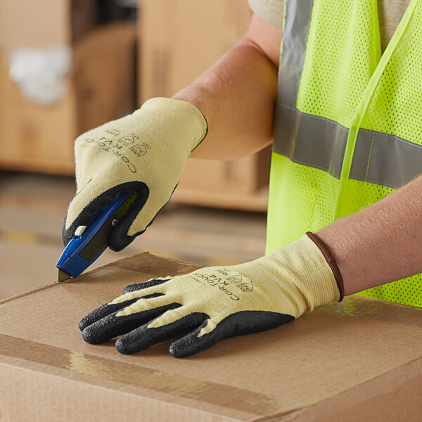 A person wearing Cordova cut resistant gloves and a safety vest using a cutter to cut a cardboard box.