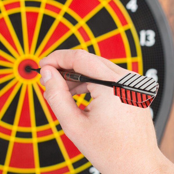A person holding an Arachnid striped soft tip dart in front of a dart board.