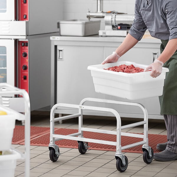 A man in a kitchen holding a Regency aluminum lug rack with a container of meat.