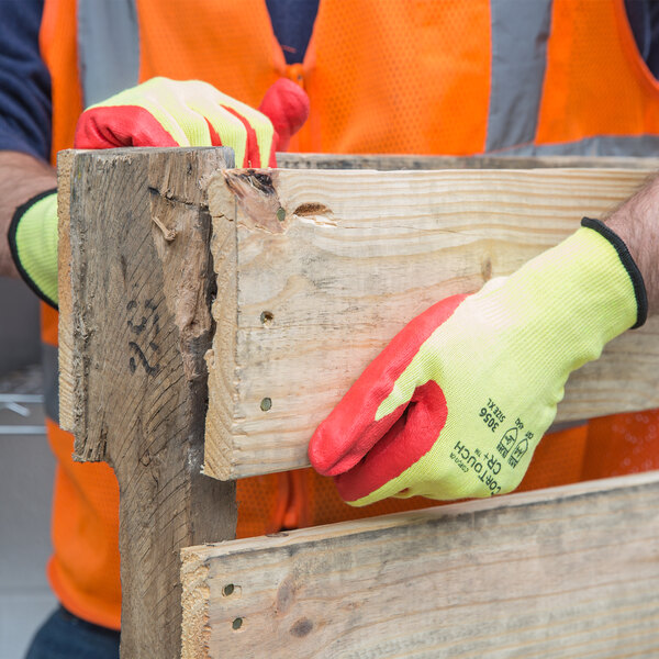 A person wearing Cordova yellow and red heavy duty work gloves holds a piece of wood.