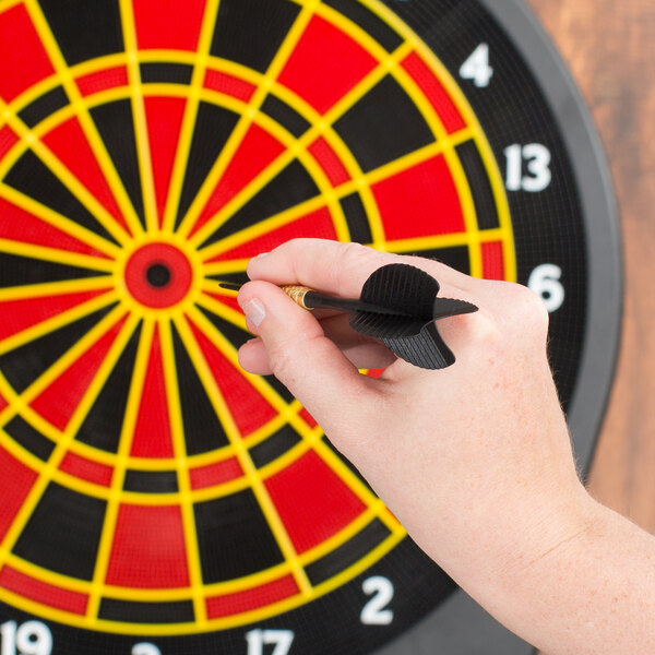 A person holding a black Arachnid soft tip dart in front of a dart board.