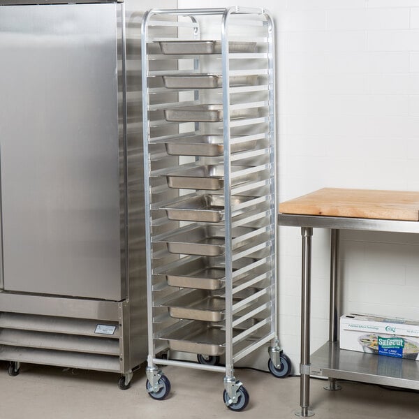 An unassembled aluminum Regency steam table pan rack filled with metal trays on wheels.
