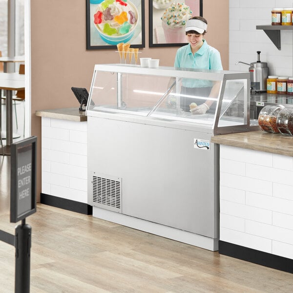 A woman standing behind a stainless steel Avantco ice cream dipping cabinet.